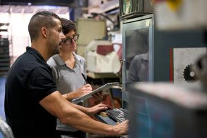 Metallurgy workers programming industrial machinery using computer in factory